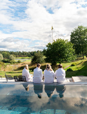 Fyra personer sitter i morgonrockar vid en utomhuspool, de blickar mot grönskande omgivningar