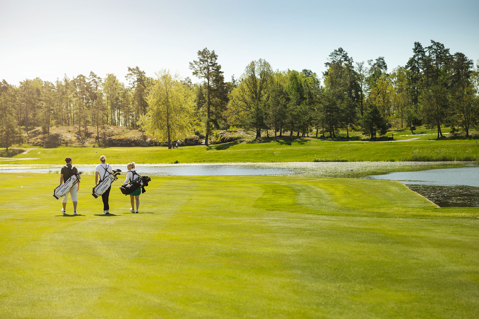 Tre människor går på golfbana