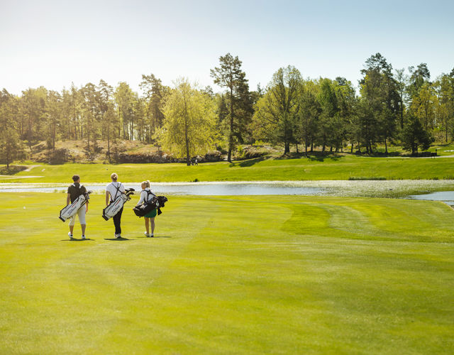 Tre människor går på golfbana