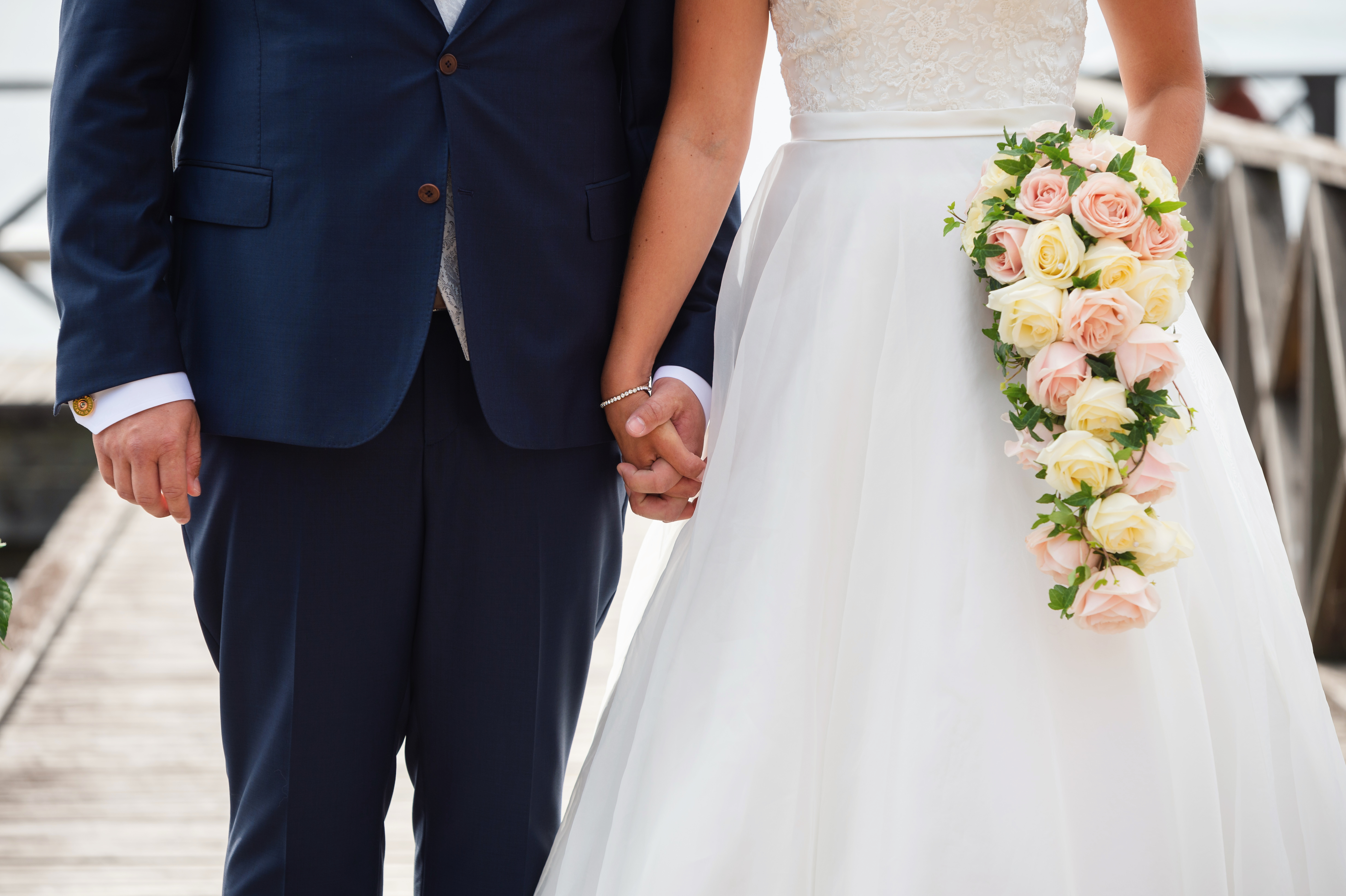 Ett bröllopspar som håller hand, iklädd bröllopsklänning och kostym