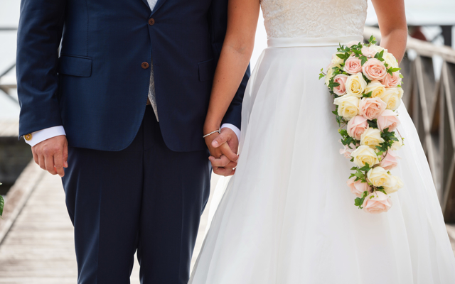 Ett bröllopspar som håller hand, iklädd bröllopsklänning och kostym