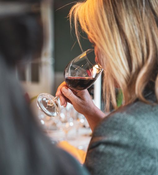 Kvinna doftar på ett upphällt rödvinsglas under en vinprovning