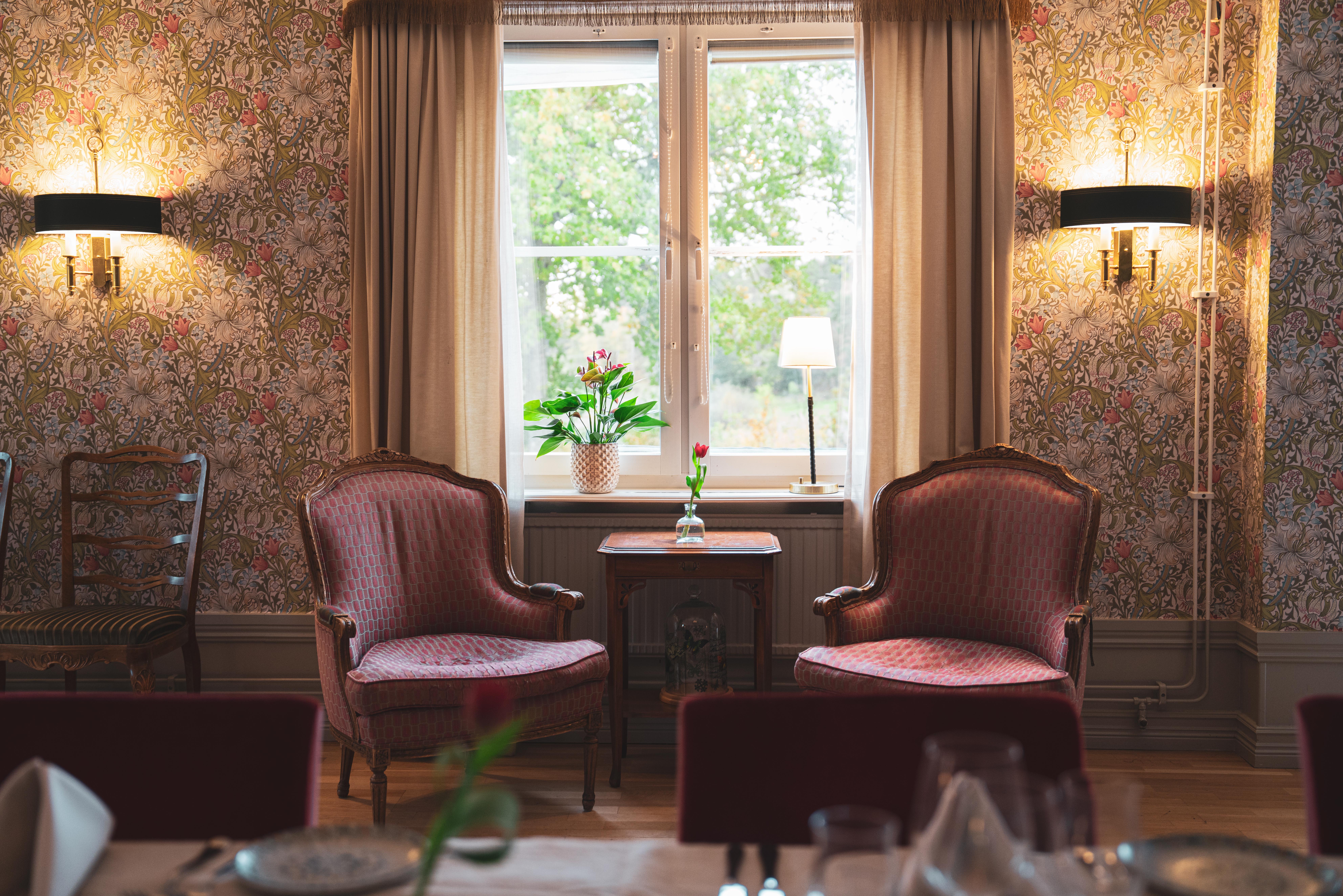 Två antika fåtöljer framför en vägg med vacker och detaljrik tapet