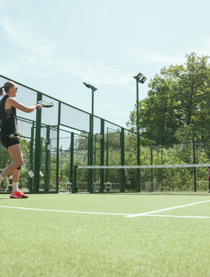Personer spelar padel utomhus på banor som omringas av grönska