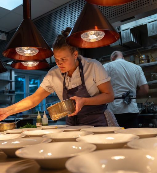Kock lägger upp mat på tallrikar i hotellets kök
