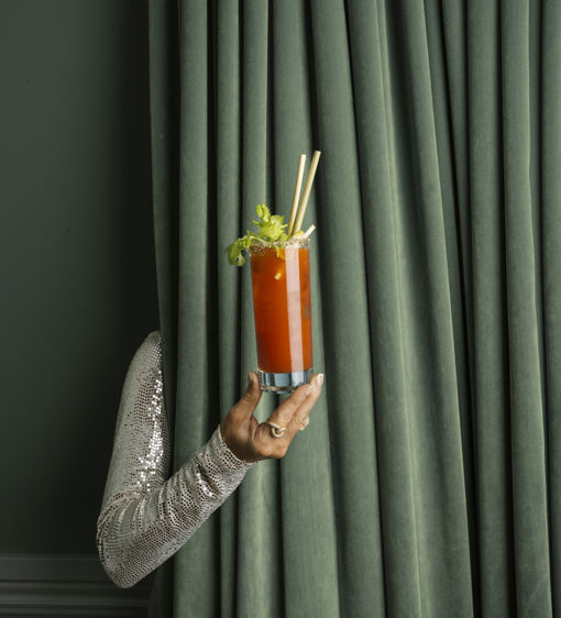 Ett glas med Bloody Mary hålls fram framför en grön gardin.