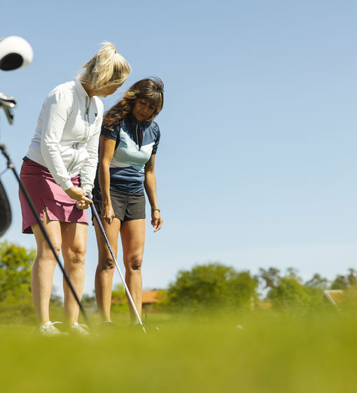 Två kvinnor spelar golf i solen