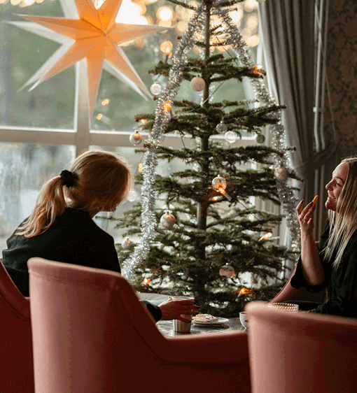 Julstämning på hotellet med julgran och julstjärna, två gäster fikar i lobbyn