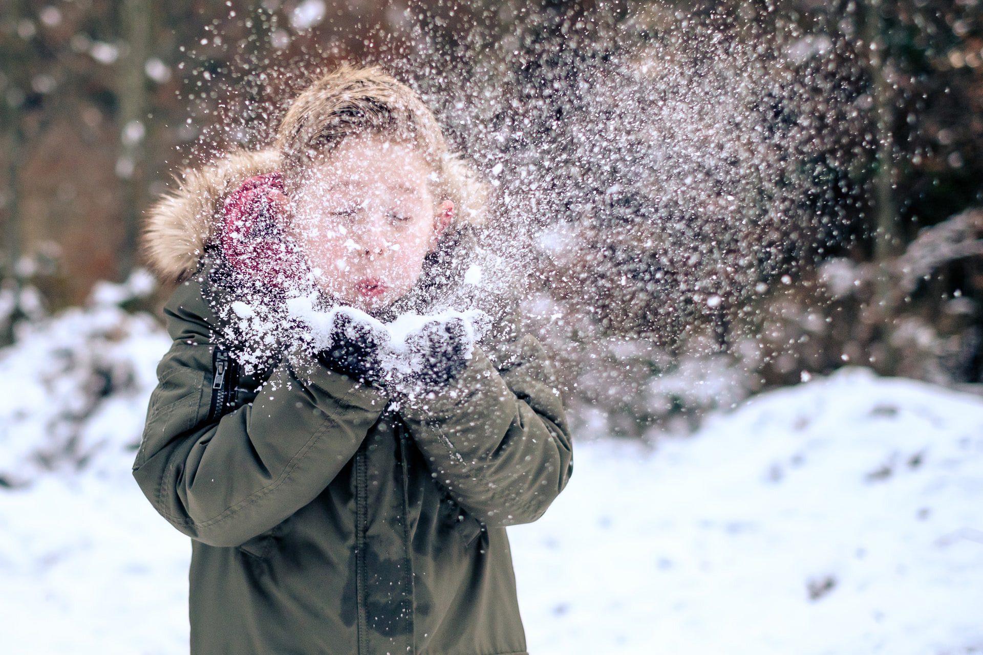 En pojke håller i snö och blåser på det så det yr ur händerna