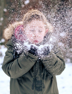 En pojke håller i snö och blåser på det så det yr ur händerna