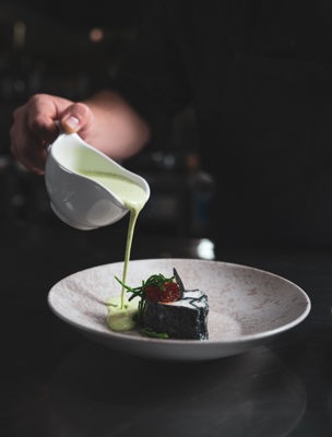 En servitör häller grön sås på en tallrik med mat