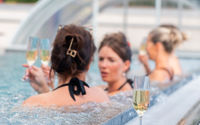 Tre kvinnor dricker champagne i en utomhuspool